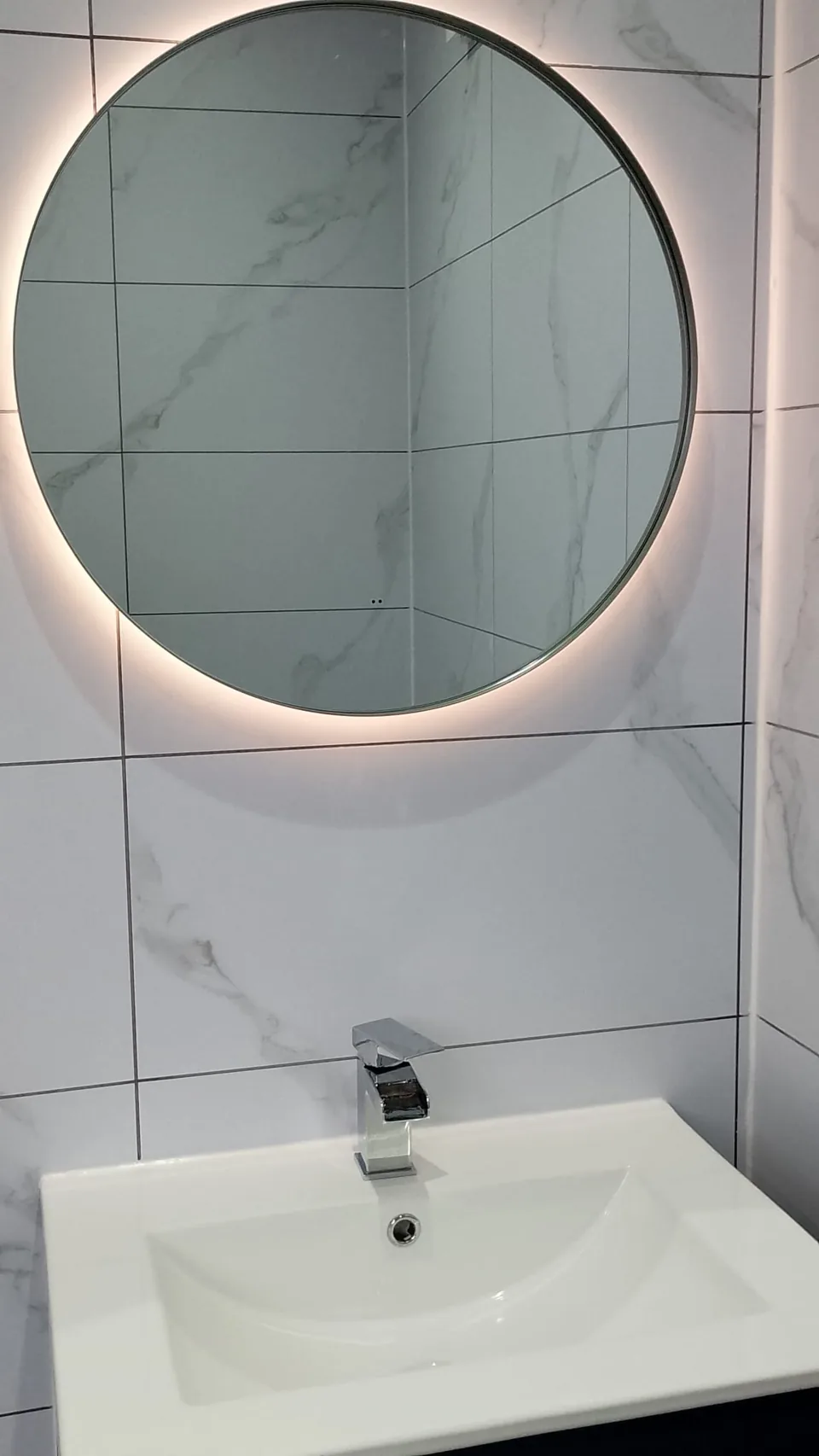 White basin beneath a round illuminated mirror